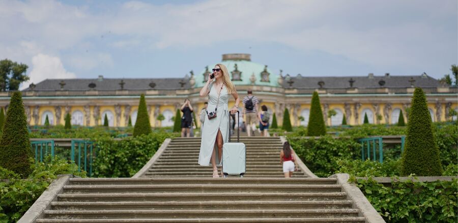 SUITLINE Suitline Banner mit Frau auf Treppe und hellem Reisegepäck vor historischem Gebäude